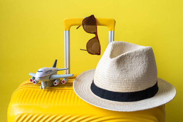 valise avec un chapeau, des lunettes de soleil et un avion sur une valise jaune contre un mur jaune. Place pour le texte. - Photo, image