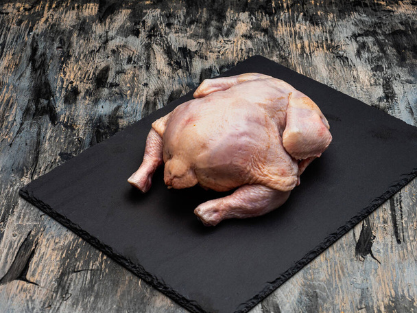 Raw domestic chicken carcass on a black slate board - 写真・画像