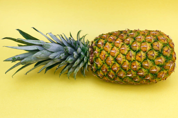 Whole pineapple fruit with top leaves placed on its left side on a paper yellow background close up. One entire complete uncut tropical fruit pineapple resting on a paper yellow background up close. - Photo, image