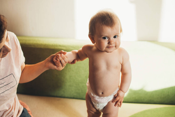 Cute little girl holding mom hand and looking at camera while standing on sofa. People lifestyle concept. - Foto, Imagen