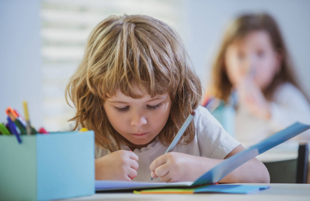 Des enfants à l'école. Un écolier écrit quelque chose dans un copybook et s'assoit à table en classe. - Photo, image