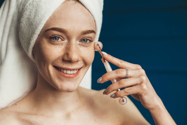 Vrouw met handdoek op het hoofd met behulp van natuurlijke jade roller voor facelifting verjonging gezicht. Glimlachend gezicht. verjongingsbehandeling. Gezichtsbehandeling, massage, huidverzorging - Foto, afbeelding