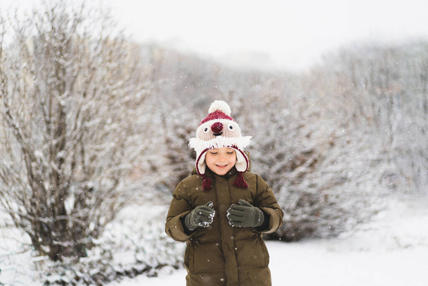 Cute little boy in funny winter hat walks during a snowfall. Outdoors winter activities for kids. - Zdjęcie, obraz