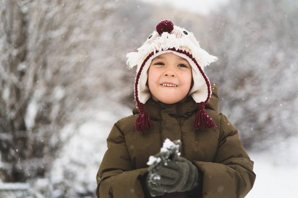 Cute little boy in funny winter hat walks during a snowfall. Outdoors winter activities for kids. - Foto, immagini