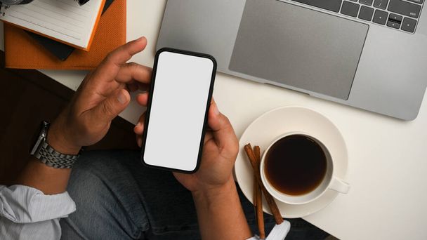 Biznesmen lub mężczyzna freelancer używa smartfona, przewijając w mediach społecznościowych w przerwie kawowej przy stole. - Zdjęcie, obraz
