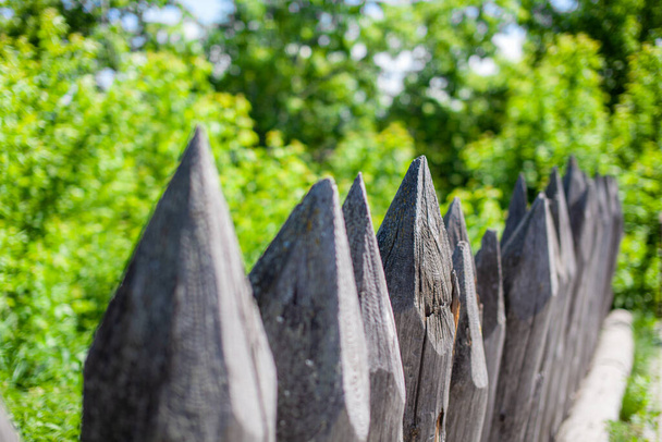 Fence made from sharp wooden stakes. Close-up on an old fence made of stakes, a picket fence, a protective structure near an old wooden fortress, selective focus - Foto, Imagen