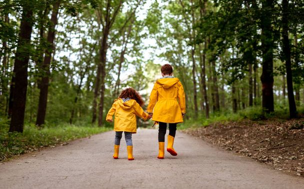Redhead siblings in yellow raincoats walking in park - Fotoğraf, Görsel