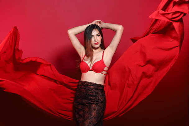 Portrét mladé štíhlé transgender asijské ženy nosí červené bikiny podprsenka šaty, Krásná dívka třepetající tkaniny házet ve vzduchu v rozdílu styl elegantní vlnový vítr, červené načervenalé pozadí - Fotografie, Obrázek