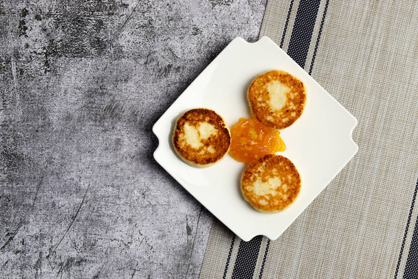 Cottage cheese pancakes with apricot jam on a white square  plate on a dark background. Top view, flat lay - Photo, Image