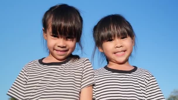 Happy Asian siblings girls hugging each other in the summer garden on a bright sky background. Portrait of smiling little girl in the park. - Video