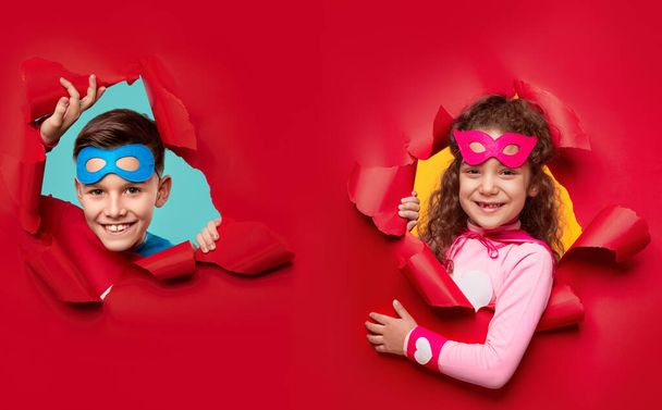 Happy superhero kids looking through torn paper - Фото, изображение