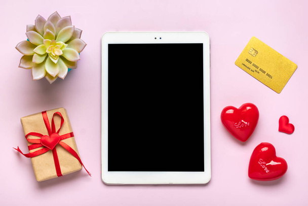 Цифровой планшет для выбора подарков, делает покупку, конверт, красные сердца на розовом столе. - Фото, изображение