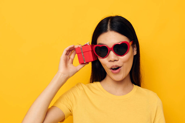 Encantadora joven asiática mujer gafas de moda regalo vacaciones amarillo fondo inalterado - Foto, Imagen