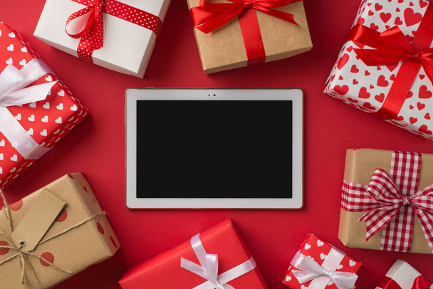Верхний вид фото день Святого Валентина украшения планшетный компьютер в окружении подарочных коробок на изолированном красном фоне с пустым местом - Фото, изображение