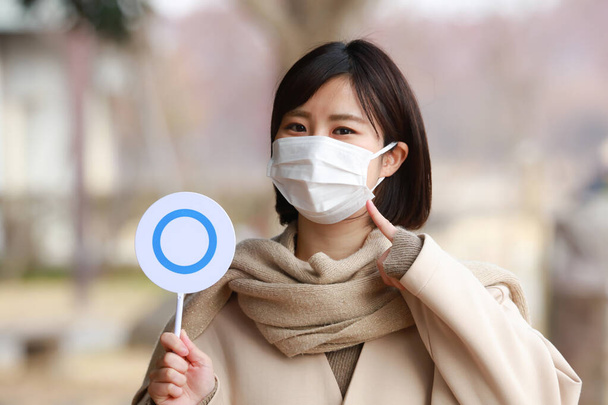 Una mujer usando una máscara y sosteniendo una etiqueta - Foto, imagen