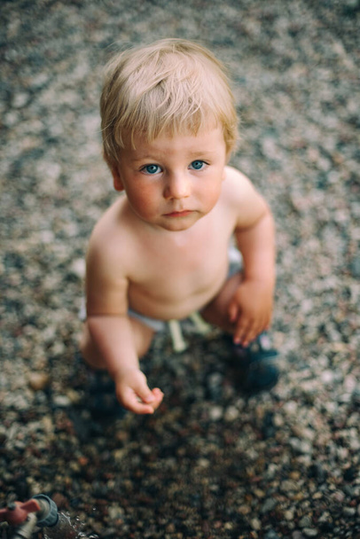 A little naked boy in the summer at the cottage drinks water from the tap. Happy carefree childhood and summer. Landscape design. Blur - Zdjęcie, obraz