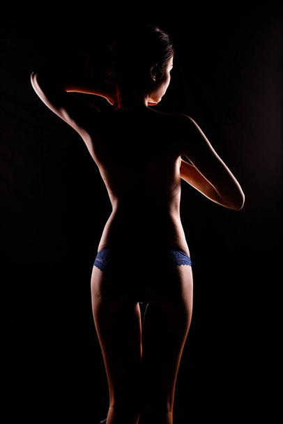 Portrait Swim wear of 20s Asian Woman in shadow low light key with back backlit, side rear view of female turn twist body for healthy shape fashion style. black background smoke exposure - Photo, image