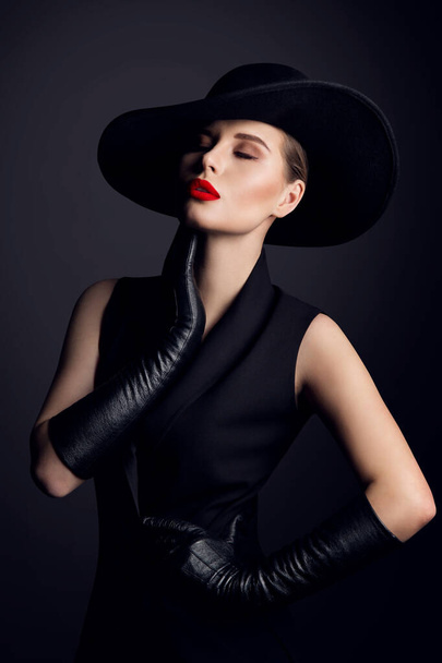 Fashion Beauty Woman Portrait in Hat with Red Lips Make up. Elegant Old fashioned Lady in Gloves dreaming with Closed Eyes over Black Studio Backgroun - Valokuva, kuva