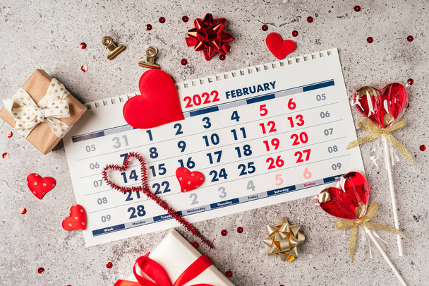 Flat lay of Valentines day calendar composition. Top view Gifts, paper, hearts confetti, ribbon, lollipops on grey table background. 14th February love concept - Zdjęcie, obraz