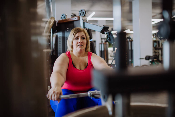 Plus size woman training on rowing machine indoors in gym - Photo, Image