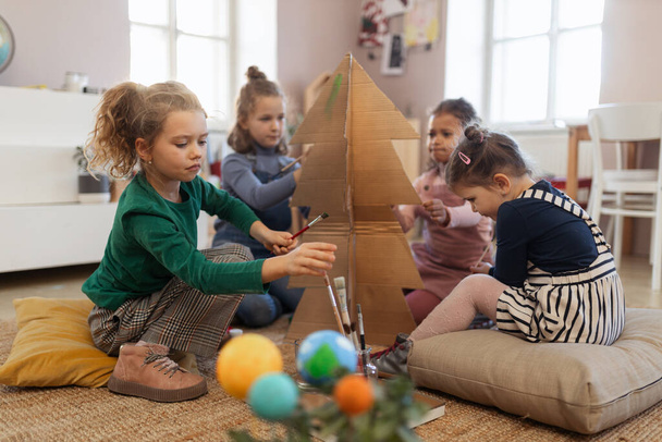 Group of little girls painting cardboard tree at creative art and craft class at school - Фото, зображення