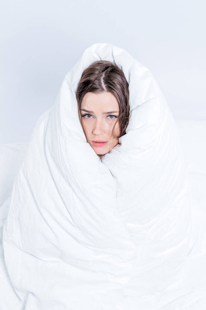 A pretty brunette is sitting on the bed, wrapped in a blanket. Keep warm with a warm blanket. Fear. Excitement. Vertical - Photo, image