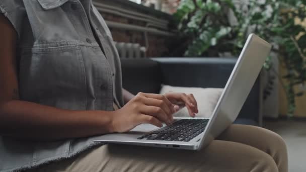 Niski kąt przyciętej kobiety siedzącej na kanapie w nowoczesnym biurze w dzień, piszącej na komputerze przenośnym - Materiał filmowy, wideo