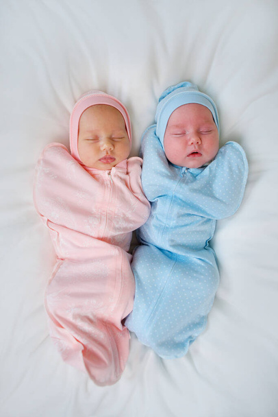 Two newborn baby twins boy and girl are in pink and blue suits on a white blanket. - Fotó, kép