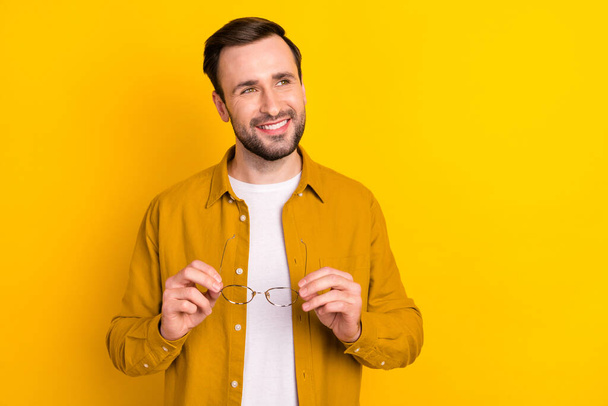 Photo of charming cute young guy wear casual clothes holding glasses smiling looking empty space isolated yellow color background. - Foto, Imagen