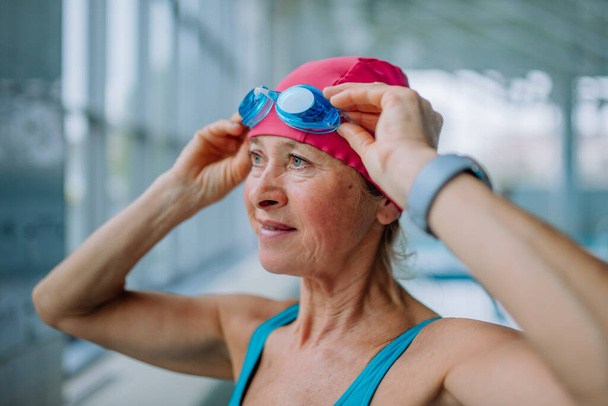 Close-up of senior woman putting on goggles before swim in indoors swimming pool. - Foto, Imagen