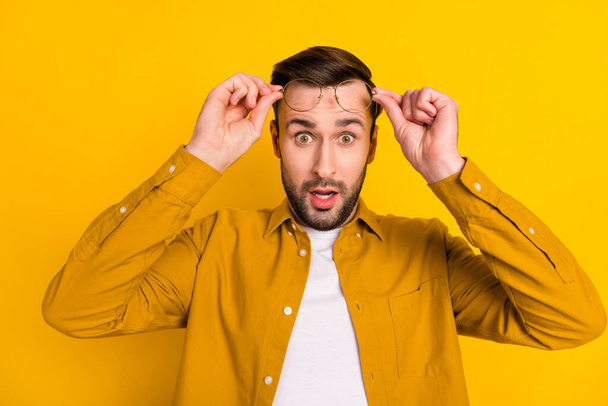 Photo of young handsome man amazed surprised shocked hands touch glasses isolated over yellow color background. - Photo, Image