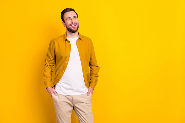 Photo of young handsome man happy positive smile hands in pocket look empty space isolated over yellow color background. - Фото, зображення