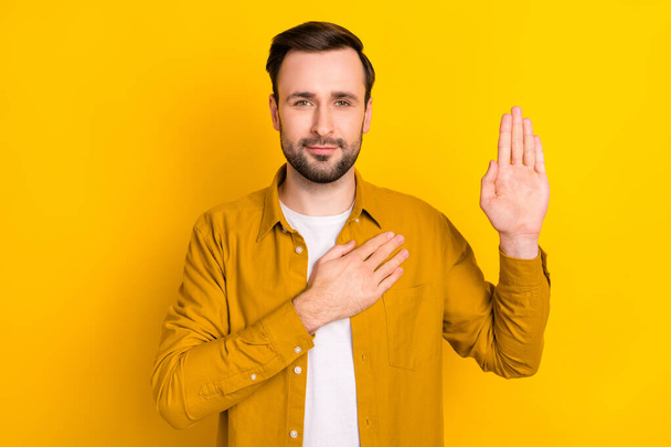 Photo of young man hands on chest make oath swear tell truth justice isolated over yellow color background. - Fotó, kép