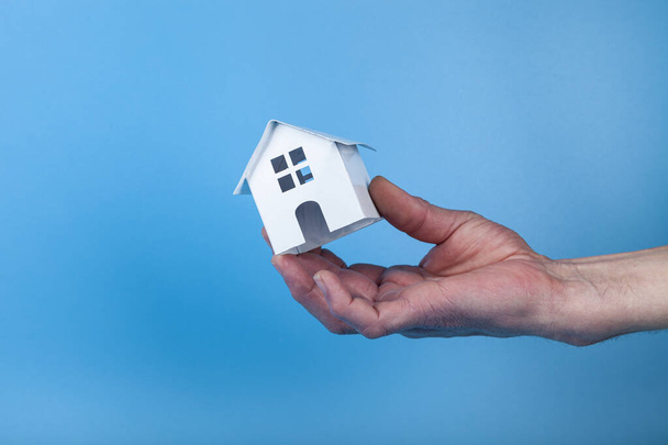 Rent apartments, Real Estate and buying a house idea. Blue background.Hand with a toy house. - Foto, Imagen