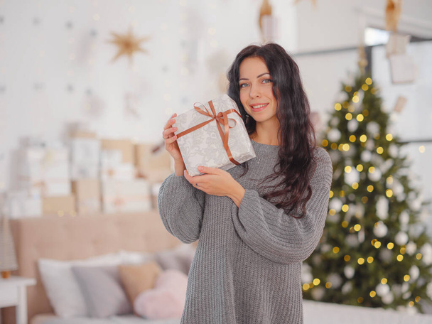 Glimlachende jonge vrouw met kerst kado doos in de buurt van kerstboom - Foto, afbeelding