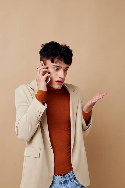 portrait d'un jeune homme vêtu d'une veste beige parlant sur le fond lumineux du téléphone inchangé - Photo, image
