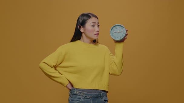 Asian woman with anxiety checking time on clock in studio - Filmagem, Vídeo