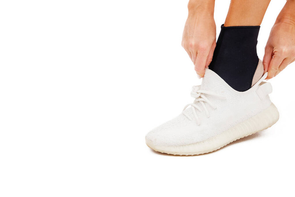 Girl puts sneakers on her leg with ankle brace on a white background - Photo, Image