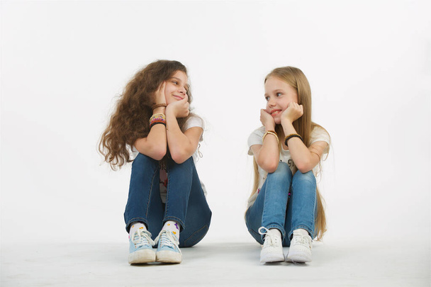 Two teen girl friends sit next to each other on an isolated white background. The girls look at each other. - Foto, Bild