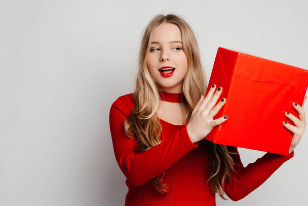 Happy woman in love celebrating Valentine's Day. Woman in red sweater with red lips holding a red present box. Giving gifts concept - Photo, Image