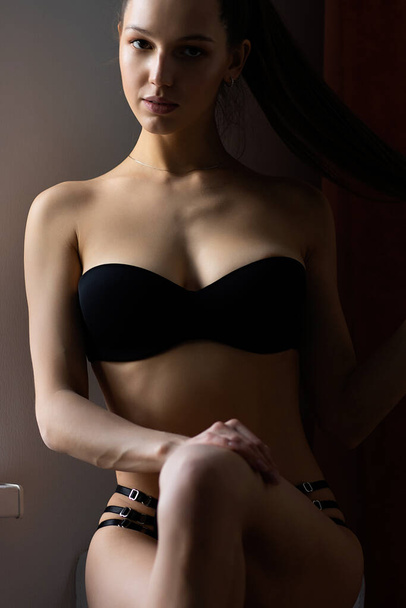 High angle of sensual slim model with long brown hair wearing black lace panties with bra sitting on bed leaning back with eyes closed - Photo, Image