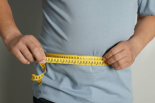 Man measuring waist with tape on grey background, closeup - Фото, изображение