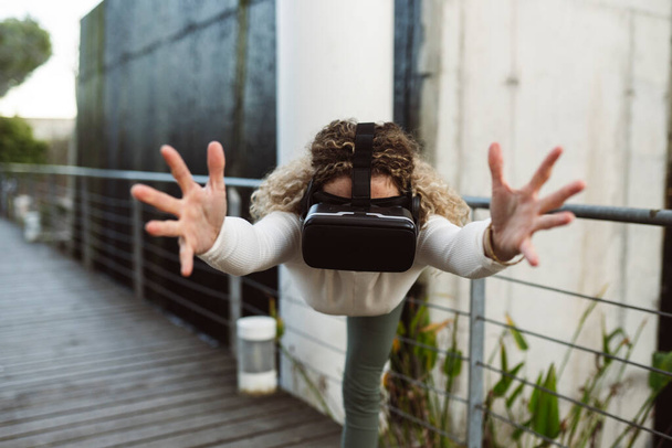 ブロンドの白人女性は、仮想現実のメガネでヨガを屋外で練習します - 写真・画像
