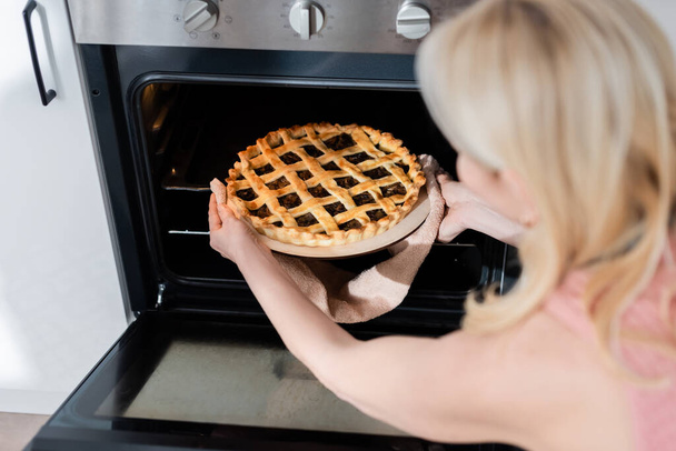 Blurred woman taking tasty homemade pie from oven in kitchen  - Fotografie, Obrázek