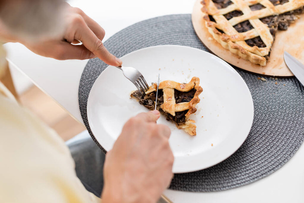 Cropped view of blurred man cutting tasty pie on plate in kitchen  - Zdjęcie, obraz