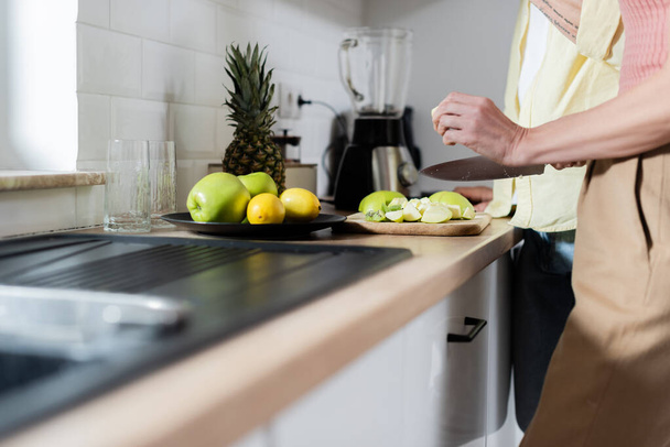 Cropped view of mature woman holding knife near fruits and husband in kitchen  - Foto, Bild