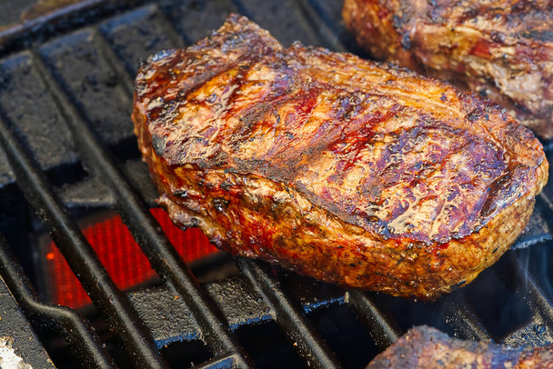 grillen steaks op brandende gas grill en geschoten met selectieve focus. Tuingrillen. Teasty steak. rib-eye steaks - Foto, afbeelding