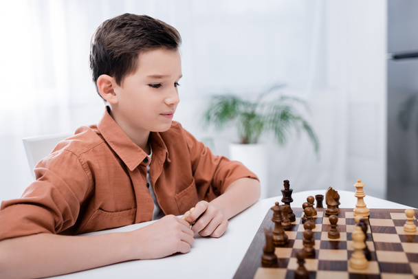 boy playing chess while sitting at table at home - Photo, Image