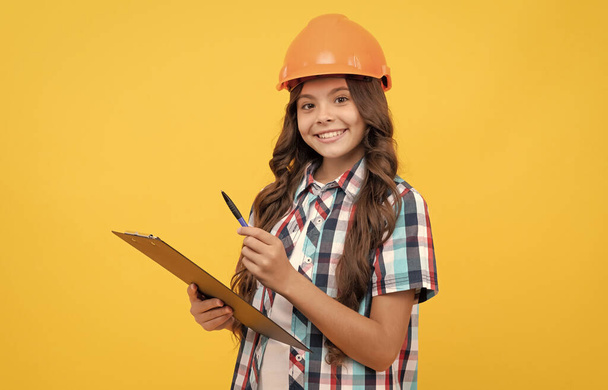 cheerful kid in construction helmet making notes in clipboard, taking notes - Photo, Image