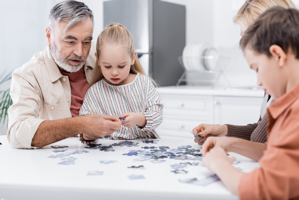 idős férfi játszik kirakós játék unokák és feleség a konyhában - Fotó, kép